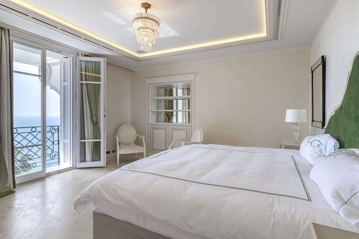 Luxurious bedroom with white bedding and a green headboard, featuring a sea-view balcony and a crystal chandelier.