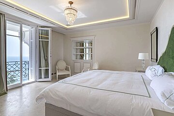 Luxurious bedroom with white bedding and a green headboard, featuring a sea-view balcony and a crystal chandelier.