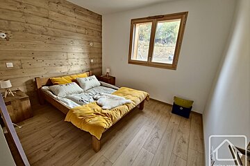 A cozy bedroom featuring a wooden bed with yellow bedding, a rustic wood plank accent wall, light wood floor, and a window overlooking outside.