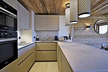 Stylish modern kitchen with light cabinetry, stone counters, built-in Miele appliances, contrasting with rustic wood ceiling & accent wall.