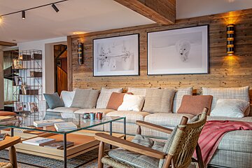 Cozy chalet living room with wooden walls, polar bear art prints, a large sofa with pillows, and a glass coffee table.