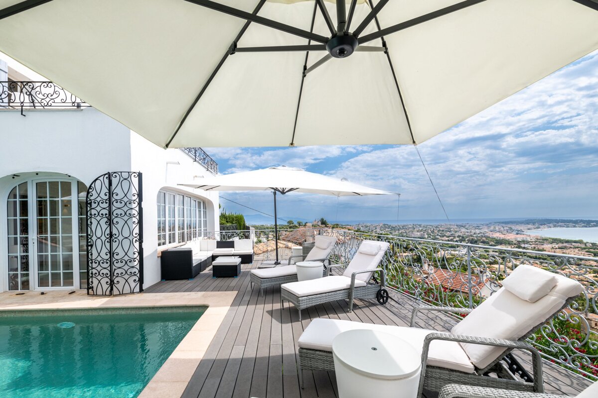 A large white umbrella is sitting on a balcony overlooking a swimming pool