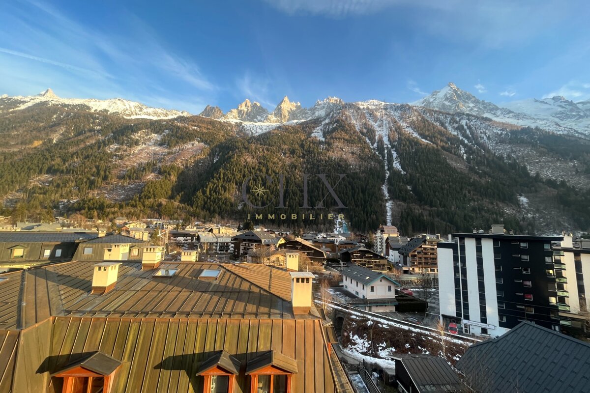Picturesque view of an alpine town with snow-dusted mountain peaks rising in the background under a clear blue sky.