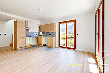 Modern open-plan kitchen/living room with light wood floors, wooden cabinets, and large windows offering a scenic mountain view.