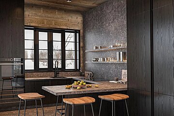 A modern, dark-toned kitchen with a rustic wood ceiling and textured grey walls. A large window overlooks a snowy landscape, complemented by bar stools and fruit.