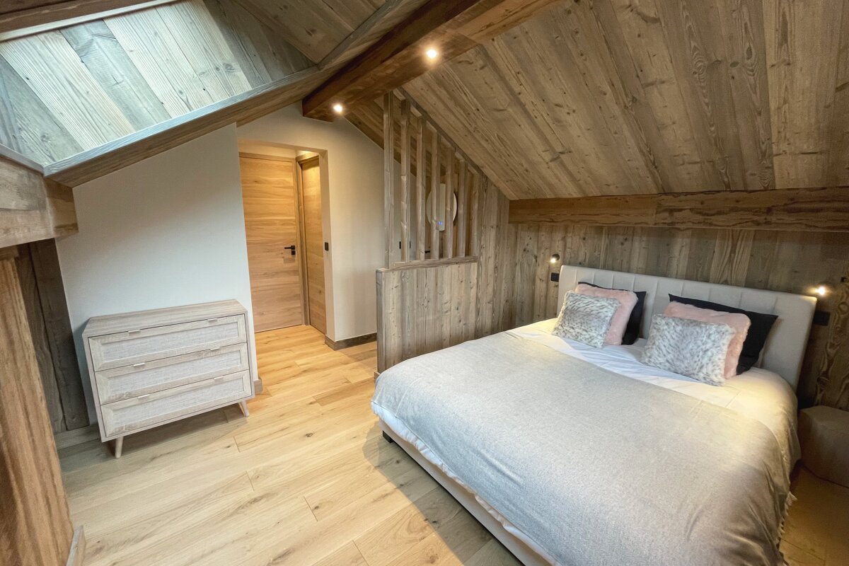 A cozy, modern attic bedroom featuring a bed, wooden walls, ceiling, and floor, a dresser, and a door, all in a warm, rustic-chic style.