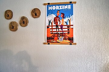 A Morzine ski poster on a textured white wall, flanked by four rustic wooden hooks.