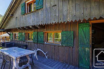 Rustic wooden chalet exterior with green shutters, a carved heart, and an outdoor dining area on its deck.