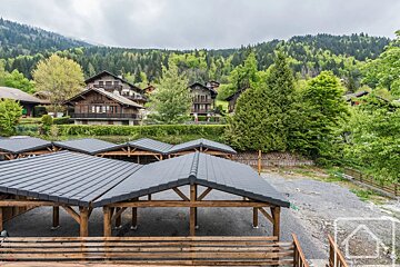 Covered wooden carports in the foreground with traditional alpine chalets nestled on a forested mountainside in the background.