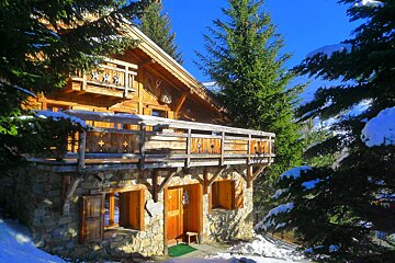 A wooden house with a balcony is surrounded by snow covered trees
