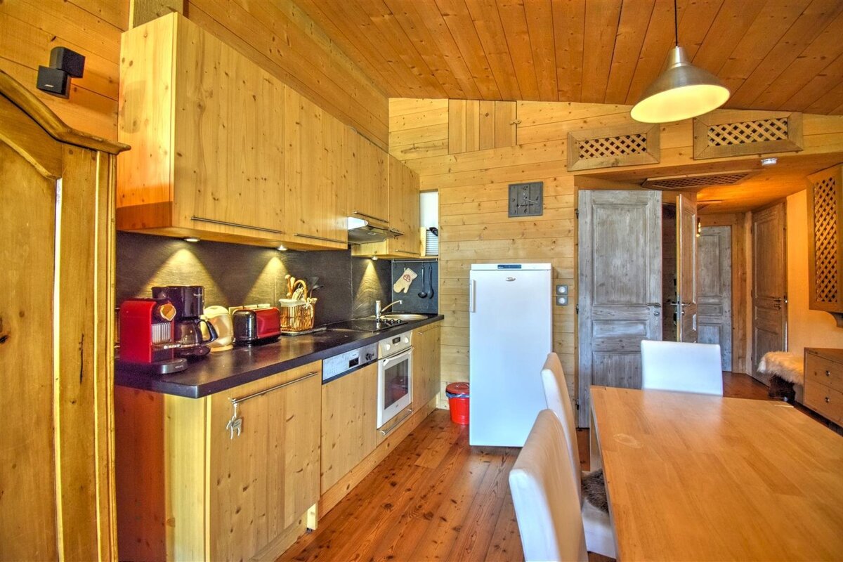 Cozy wooden cabin kitchen and dining space with natural pine cabinetry, a white refrigerator, and a wooden dining table.