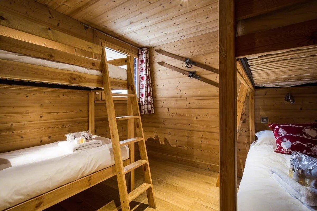 Cozy wooden ski chalet bedroom featuring bunk beds and vintage skis mounted on the wall.