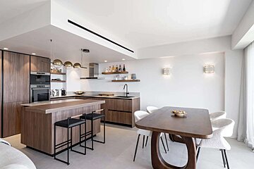 A modern open-plan kitchen and dining area with warm wood cabinets, a spacious island, white walls, and contemporary furniture.