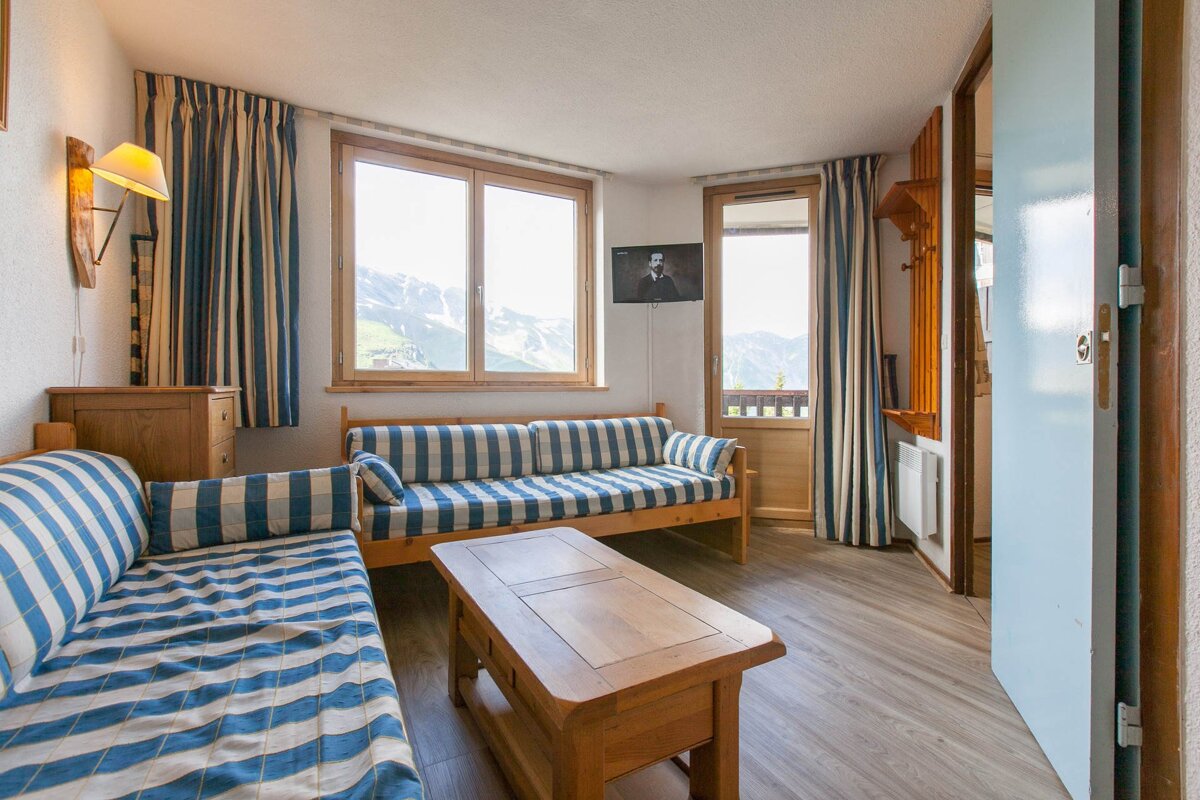 A cozy living room with blue & white striped seating, a wooden coffee table, and mountain views from windows and a balcony.