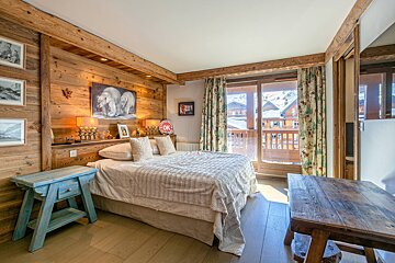 Cozy wooden chalet bedroom with a large bed, polar bear artwork, and a balcony overlooking a snowy alpine village.