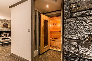 A wooden sauna is next to a stone wall