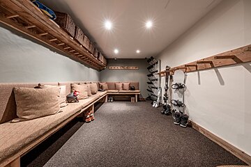 A rustic ski/mudroom with long cushioned benches, wooden shelves & baskets, and organized racks for skis, snowboards, boots, and helmets.