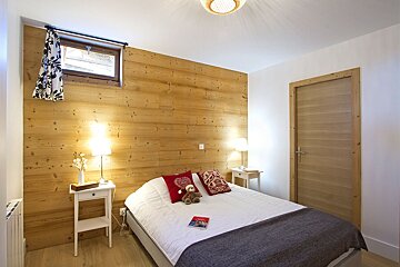 A bedroom with wood paneling and a bed with a teddy bear on it