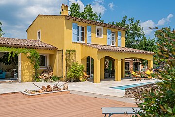 A yellow house with blue shutters sits next to a pool