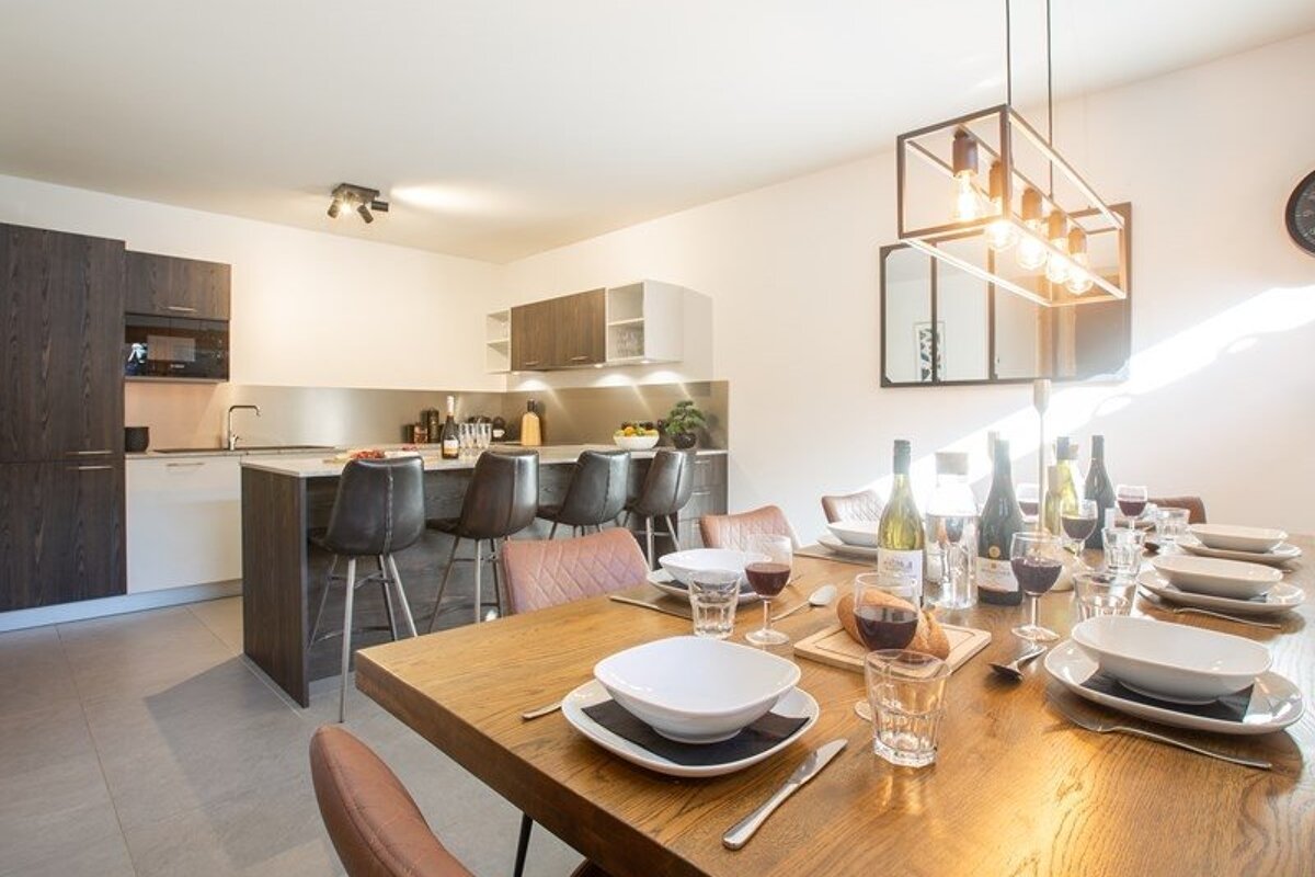 A modern open-plan dining room and kitchen, featuring a beautifully set wooden table and a stylish island with bar stools.