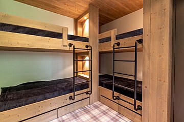 Two modern rustic wooden bunk beds with industrial black ladders and dark bedding are arranged in an L-shape, featuring a cozy plaid carpet.