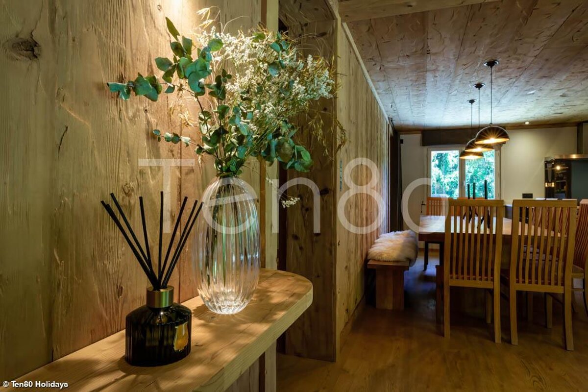 A vase of flowers sits on a wooden shelf in front of a sign that says ten80 holidays