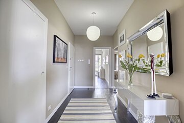A contemporary hallway with light walls, dark floors, striped rug, console table, mirror, flowers, and a round pendant lamp.