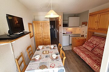 A well-organized studio apartment with a dining table, equipped kitchenette, sofa bed, TV, and warm wooden furniture, suggesting a compact holiday rental.