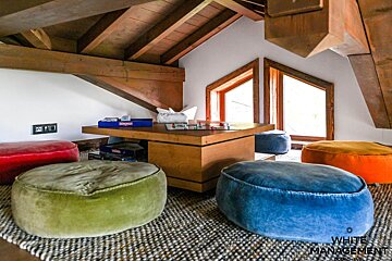 Cozy attic playroom with colorful velvet floor poufs surrounding a low wooden table with board games under exposed beams.