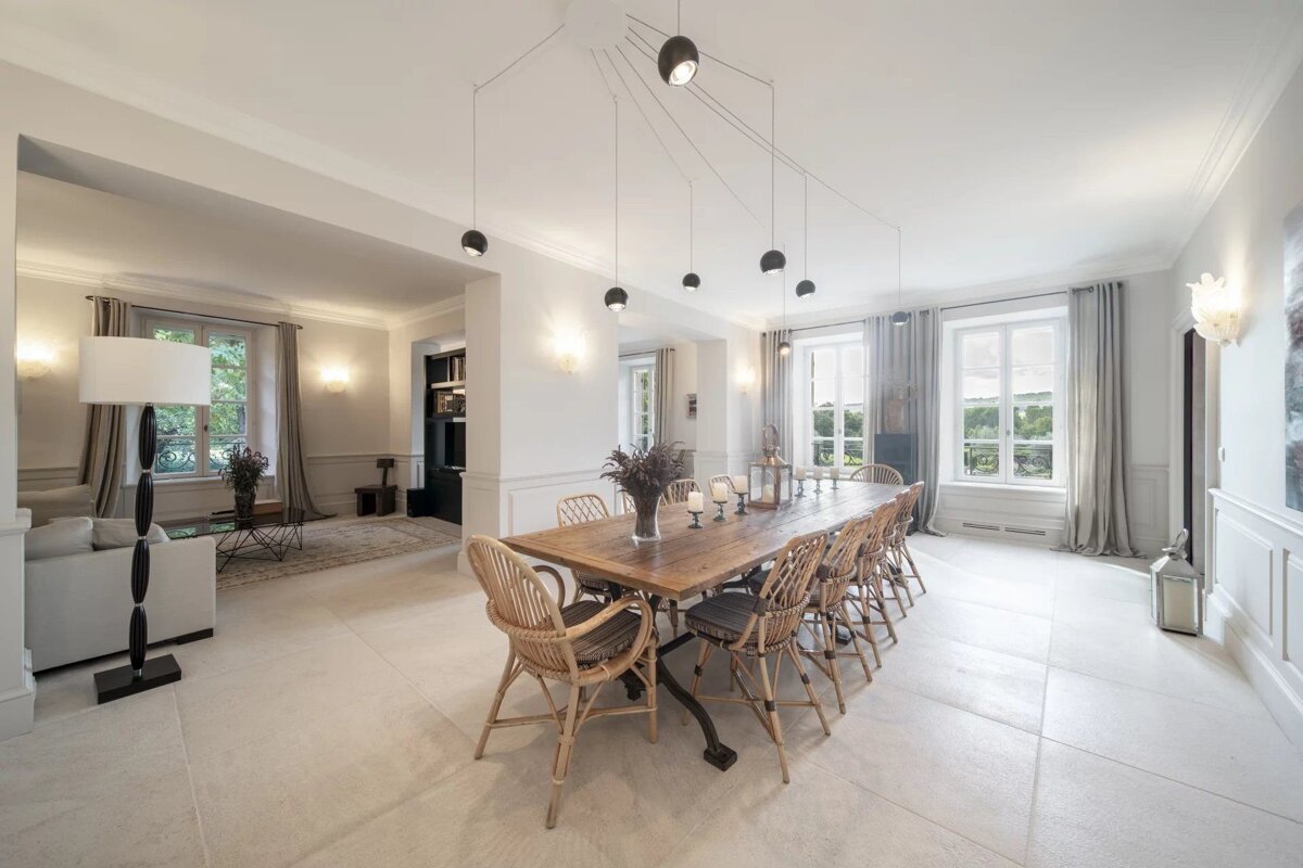 Bright, spacious dining room featuring a long wooden table, wicker chairs, and minimalist black pendant lights.