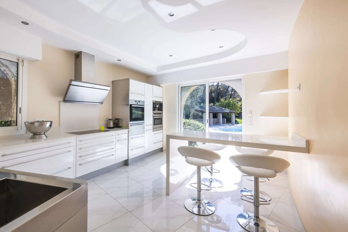 A sleek, modern kitchen with white cabinetry, stainless steel appliances, a breakfast bar, and a bright view of an outdoor pool.