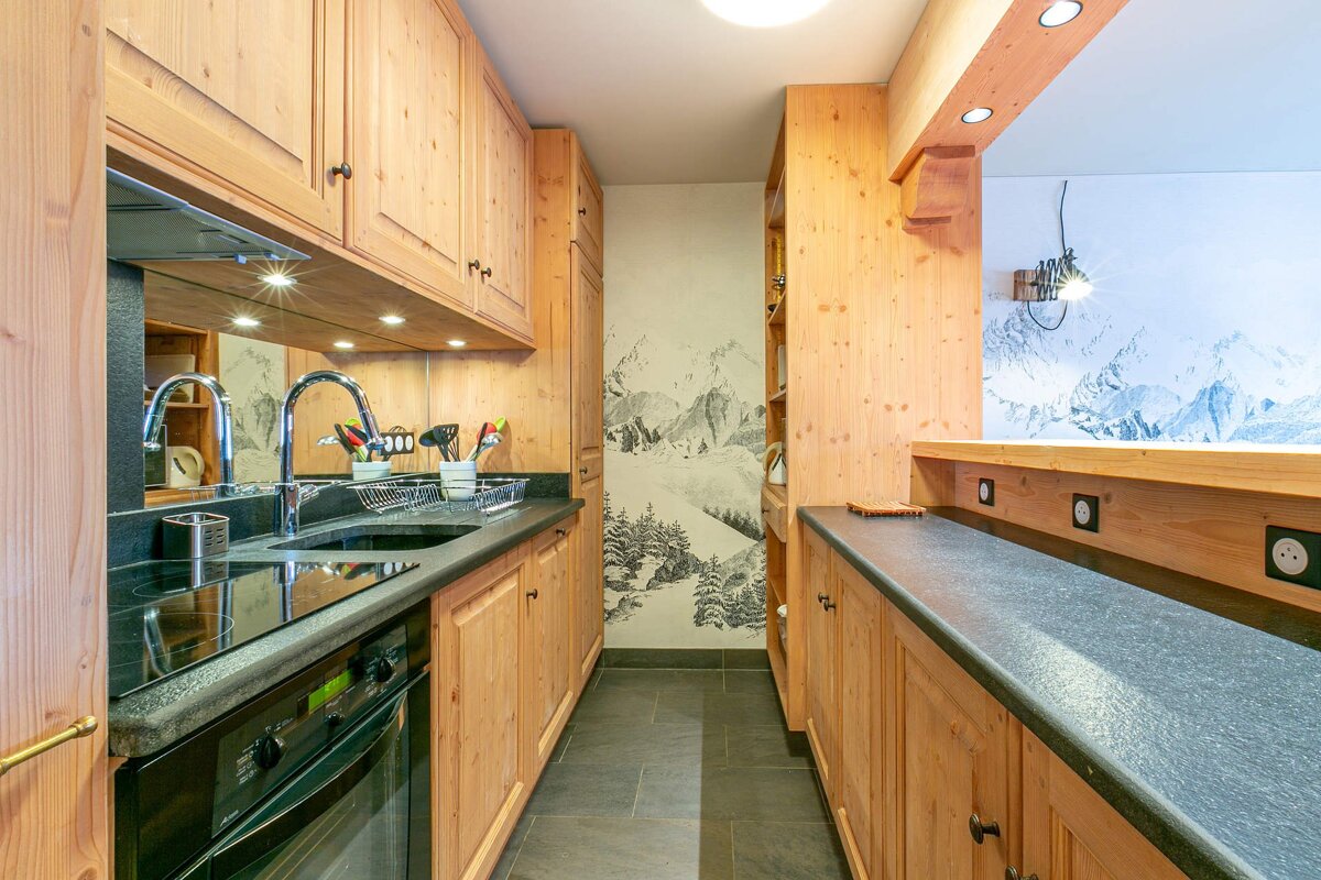 A rustic-chic kitchen with natural wood cabinets, dark grey countertops, and a striking mountain-themed mural, offering a warm and functional space.