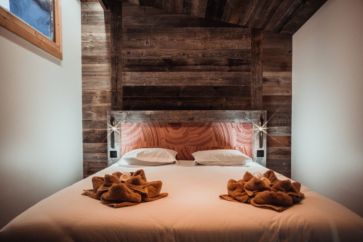 Cozy rustic bedroom with a wood-paneled wall, a bed with folded decorative towels, and warm side lights.