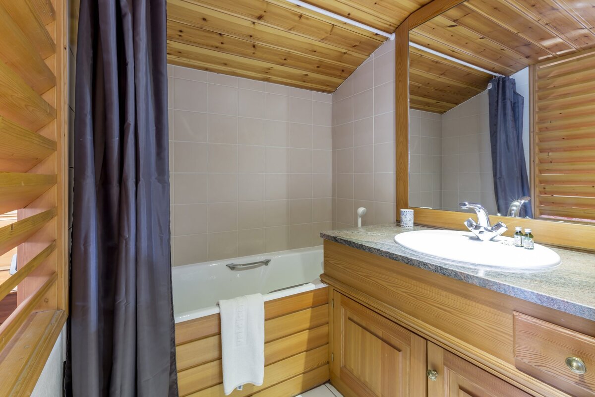 Wood-paneled bathroom with a bathtub, shower curtain, tiled walls, and a sink vanity with a mirror.