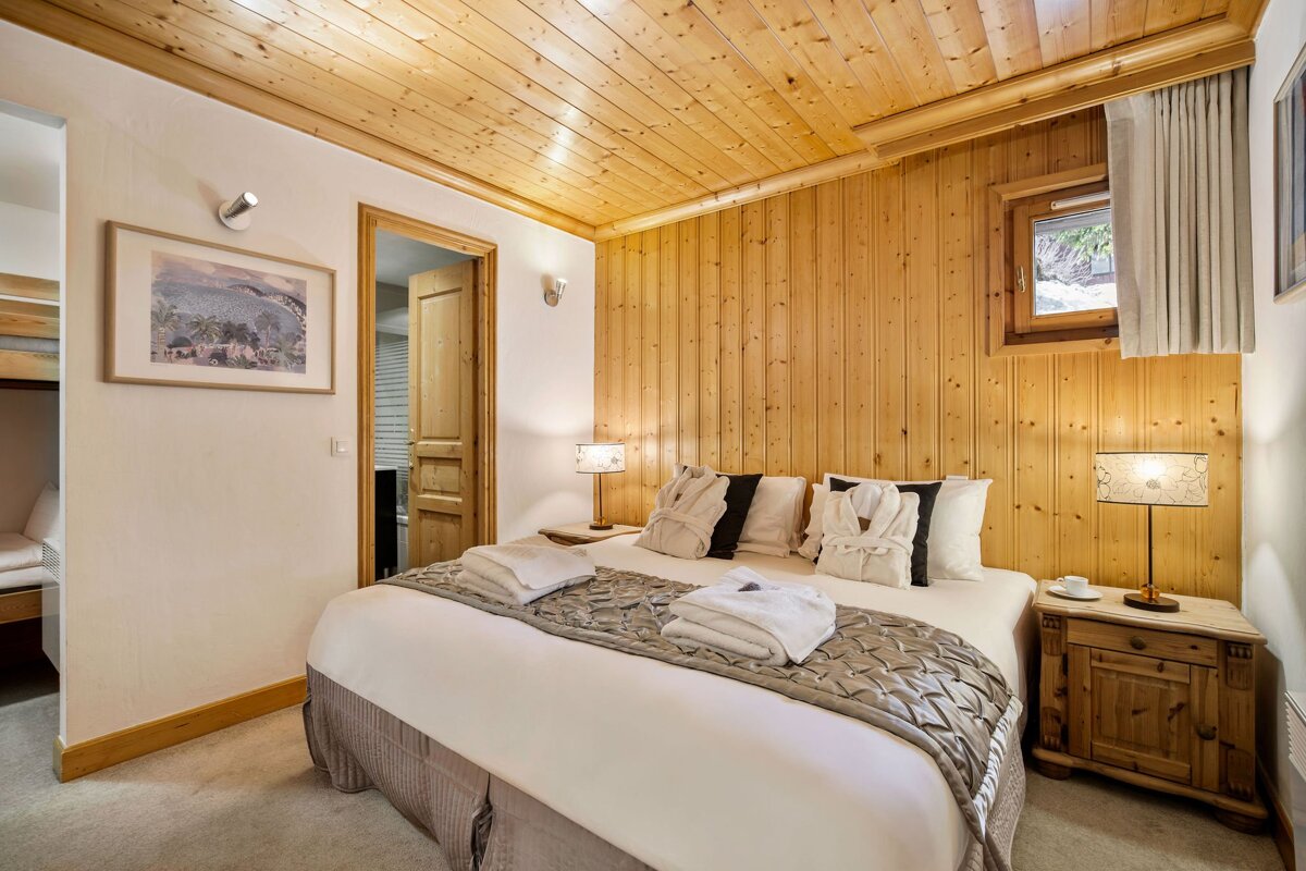 Cozy chalet bedroom featuring a large bed with white linens, rustic wood-paneled walls and ceiling, and warm bedside lighting.