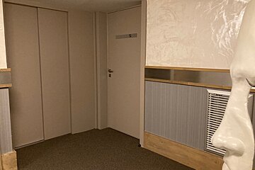 A hallway corner with closed beige doors, textured walls, a vent, and a partial view of a white face sculpture in the foreground.