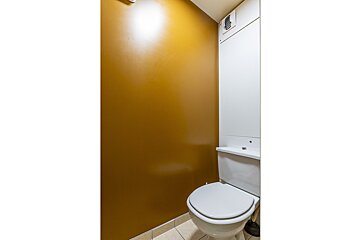 A toilet with a yellow wall behind it
