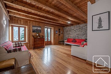 Cozy, rustic living room with wooden walls, beamed ceiling, stone accent wall, red sofas, and a snowy window view, evoking an alpine feel.