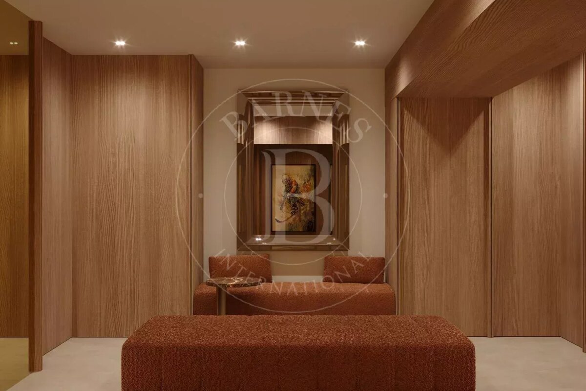 A stylish hallway with light wood paneling, recessed lights, and rust-colored seating. A framed abstract painting hangs above a built-in bench.