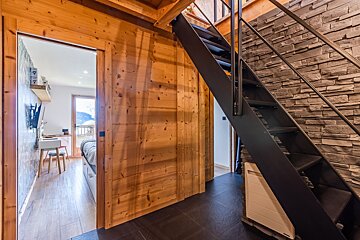 Rustic modern cabin interior featuring a black metal staircase next to a stone wall, with a doorway opening into a bedroom.