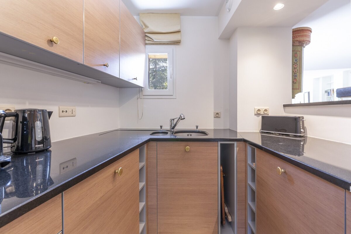 A small, modern kitchen featuring light wood cabinets, sleek black countertops, a sink, and black appliances.
