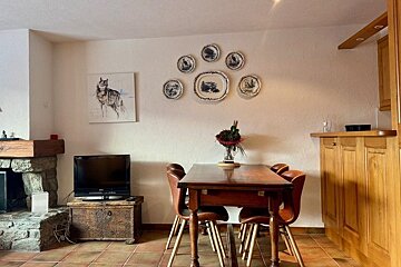 Rustic dining area with a wooden table, chairs, decorative wall plates, a wolf painting, and a TV on a chest next to a stone fireplace.