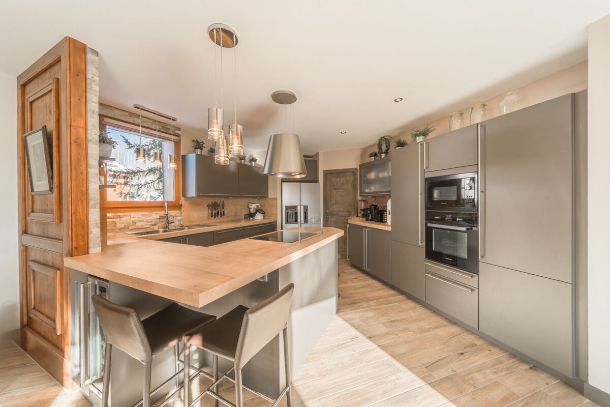 Modern gray kitchen with wooden countertops, an island with bar stools, sleek appliances, and warm wood flooring.