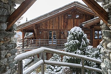 A wooden house with a balcony is covered in snow