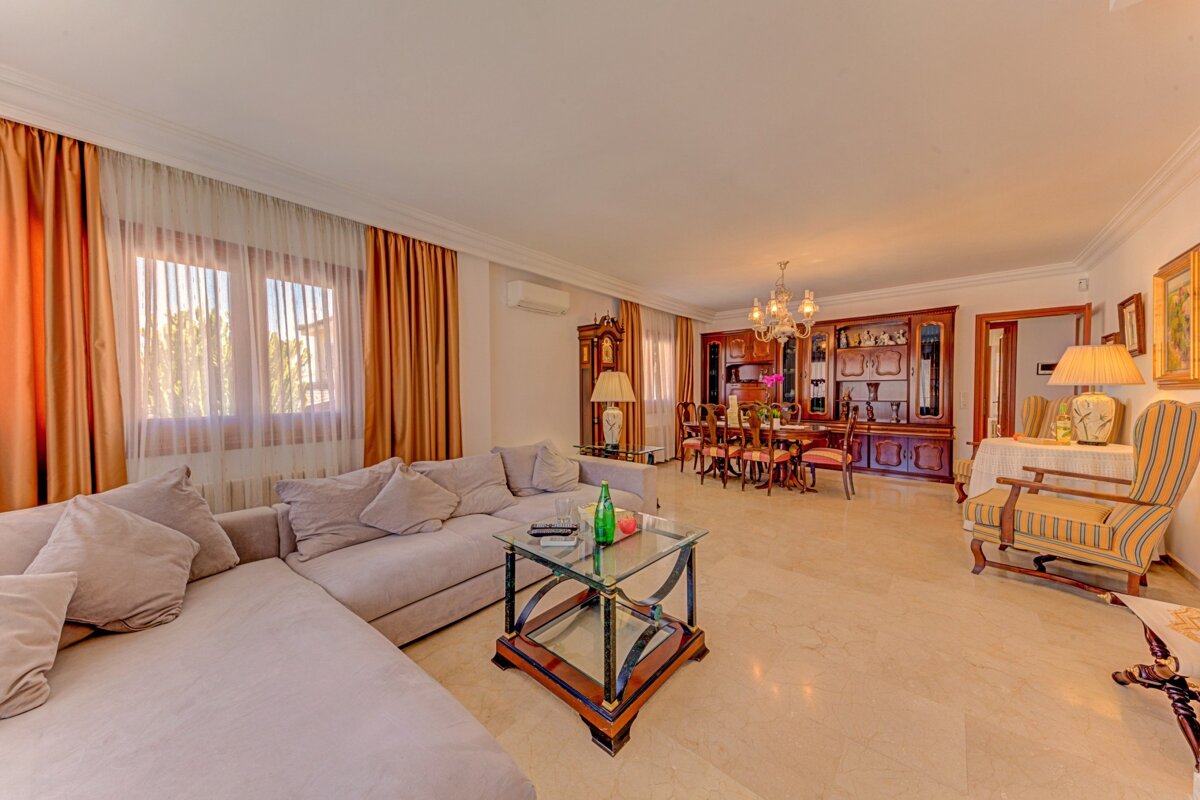 An elegant living/dining room features an L-shaped sofa, glass coffee table, formal dining set, marble floors, and long orange curtains.