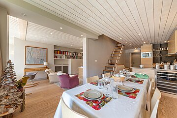 Bright open-concept living space featuring a set dining table, a cozy sitting area, kitchen, and wood-paneled ceilings.