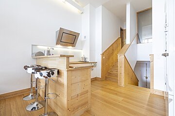 Modern apartment interior featuring a wooden kitchen bar with cow-print stools next to wooden staircases.