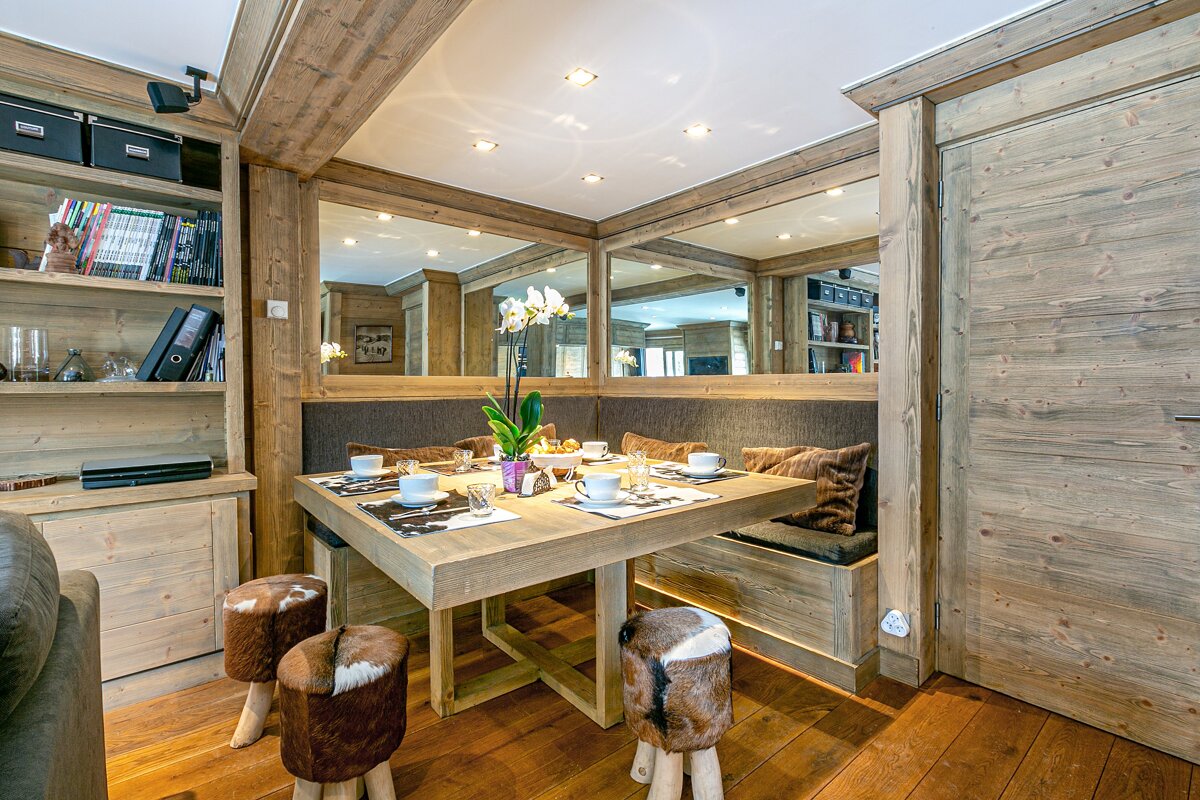 Rustic wood dining nook with built-in bench seating, a set table, and unique fur stools. Mirrors create depth in this cozy, chalet-style space.
