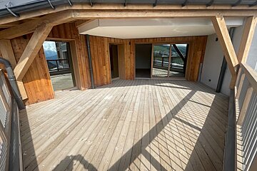 A spacious wooden balcony of a chalet featuring a large deck, paneled walls, and sliding glass doors.