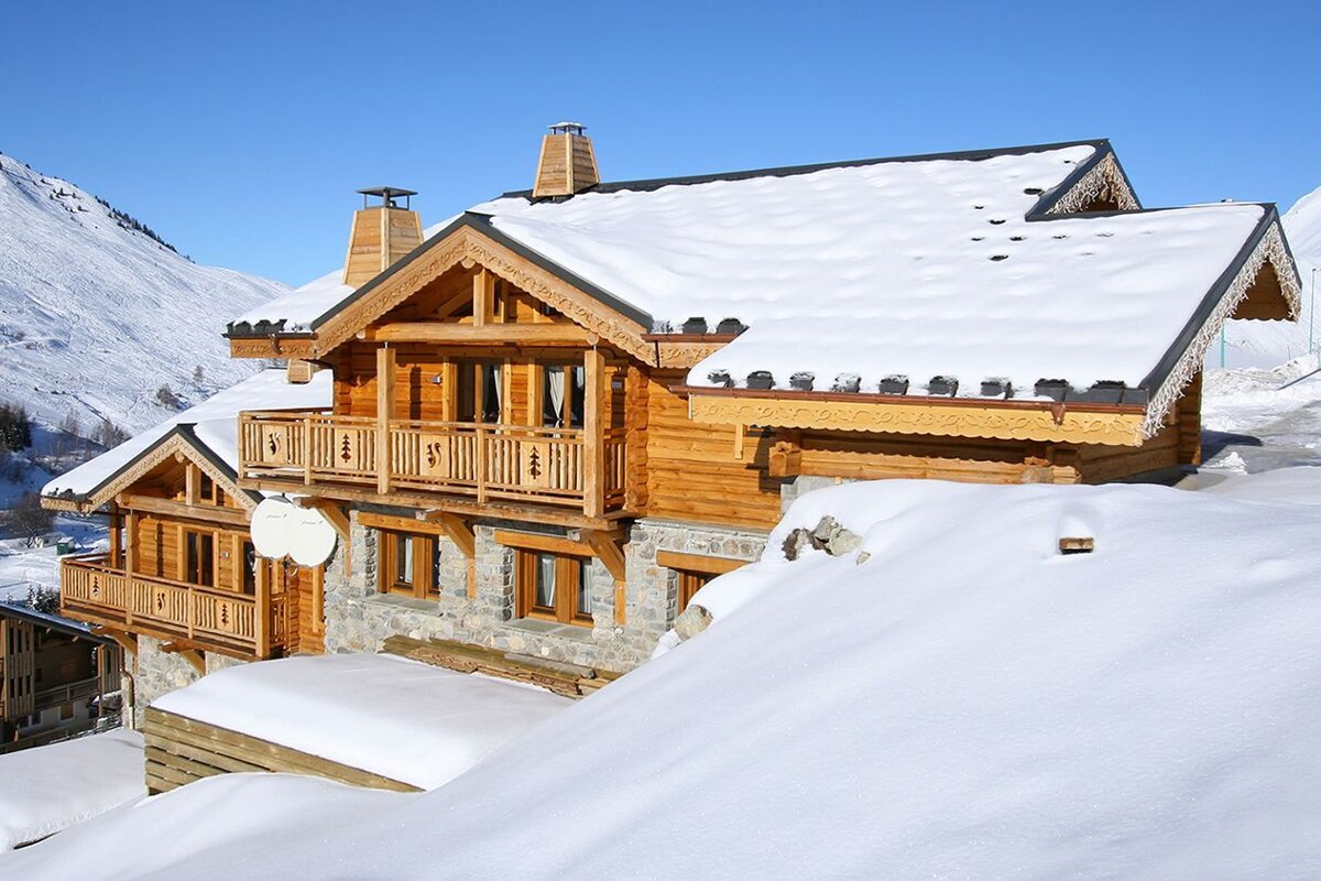 A wooden house with a balcony is covered in snow